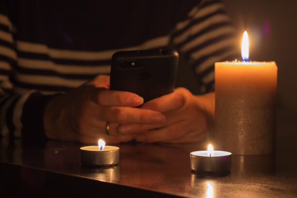 Mobile,Phone,In,Hands,And,Burning,Candles.,Blackout,Due,To