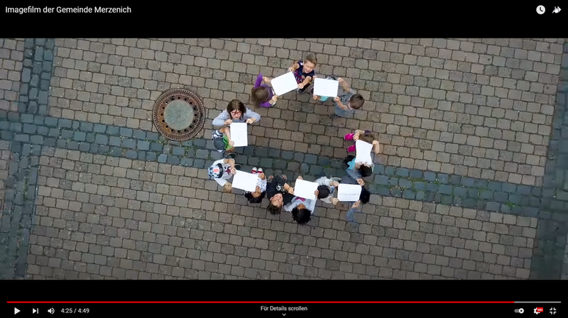 Kinder stehen im Kreis und halten Papierblätter über sich. Von oben gefilmt